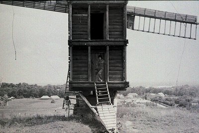 Vintage black-and-white photo of a wooden watchtower with a ladder and elevated platform, likely a lookout or signal post. A ...