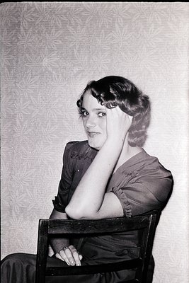 Portrait of a woman in 1930s–1940s fashion: pinched waist dress, curled hairstyle, and vintage floral wallpaper backdrop. Cla...