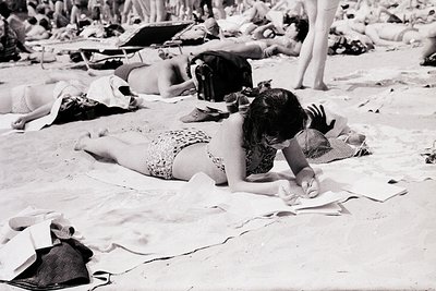 Mid-20th century beach scene with relaxed, sunbathing figures in swimwear. A woman in patterned bikini and sunglasses sits wr...