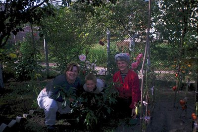 Three adults pose in a lush garden with vibrant blooms and greenery, likely mid-20th century. The woman on left wears a patte...