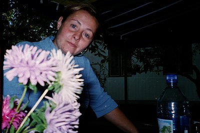 Portrait of a woman holding a bouquet of pink chrysanthemums, likely mid-1990s–2000s. Indoor setting with floral-patterned wa...