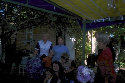 Family portrait under a covered patio with lush greenery. Three adults and two children pose in vintage clothing—1970s style....