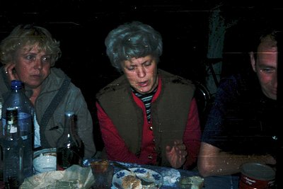 Vintage candid shot of three individuals seated indoors, likely mid-1970s Eastern Europe. Central figure wears a striped swea...