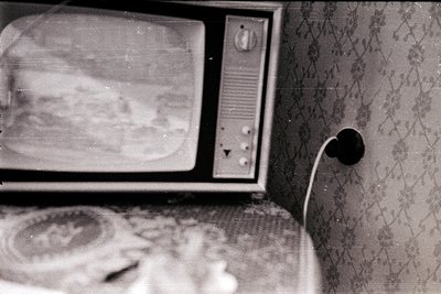 Vintage CRT TV with worn screen and floral-patterned wallpaper, likely mid-20th century. Knob and antenna suggest analog broa...