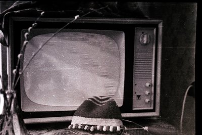 Vintage CRT television with blurred screen, placed on a dark surface. A knitted hat with a pom-pom rests on the lower left co...