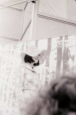 Vintage black-and-white portrait of a woman in a wide-brimmed hat and floral blouse, shielding her eyes with one hand. Soft f...