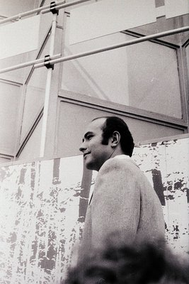 Mid-century modern interior with clean lines and geometric ceiling supports. Man in a light scarf or shawl, posed indoors, li...