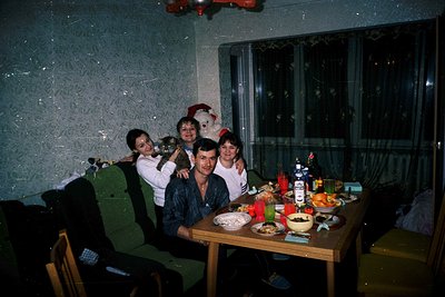 Family gathering in a Soviet-era apartment during the 1970s–1980s, likely Eastern Bloc. Indoor setting with textured wallpape...