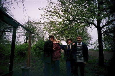Vintage group portrait under a rustic wooden pergola in a lush, overgrown garden. Four individuals pose with casual 1970s-80s...