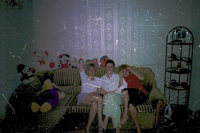 Vintage group portrait on a striped sofa, likely 1970s–1980s. Three individuals pose with playful expressions, surrounded by ...