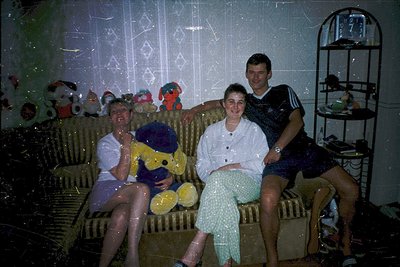 Vintage indoor portrait of four people on a couch, likely from the 1970s–1980s. The setting features retro decor: patterned w...