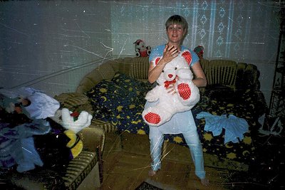 Vintage indoor portrait of a child in a 1970s-style teddy bear costume, holding a plush bear with red polka-dot accents. The ...