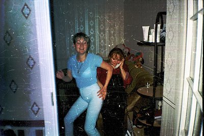 Reflection-captured moment in a retro interior: two women in mirrored doorway, one in light blue tracksuit, the other in dark...