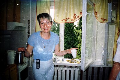 Vintage indoor kitchen scene featuring a woman in a light blue shirt and matching pants, holding a mug while standing beside ...