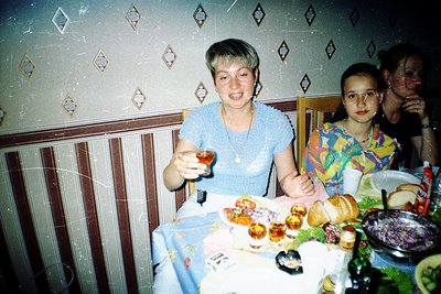 Vintage indoor family gathering with two women at a table laden with pastries, bread, and a bowl of fruit. Decor includes geo...