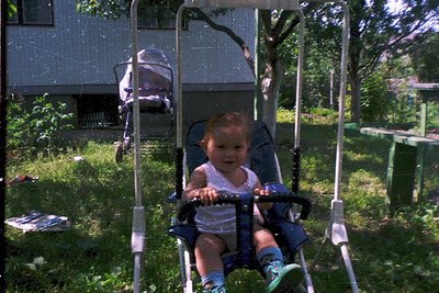 Vintage swing set with child seated in a plastic bucket-style seat, wearing a white sleeveless top and striped socks. Residen...