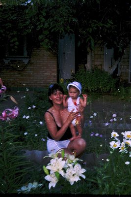 Vintage photo of a woman and infant playing in shallow water surrounded by lilies and pink flowers. Mid-20th century summer a...