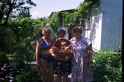 Vintage family portrait in a lush garden, likely Eastern Europe, 1970s. Three women in retro swimwear and floral dresses pose...