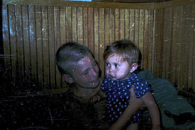 Vintage black-and-white photo of two children peering through a wooden slatted window. The boy, older, leans in close to the ...