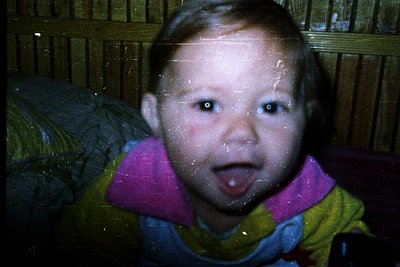 Vintage-style photo of a young child in a striped sweater and scarf, taken through a frosted glass window. The soft focus and...
