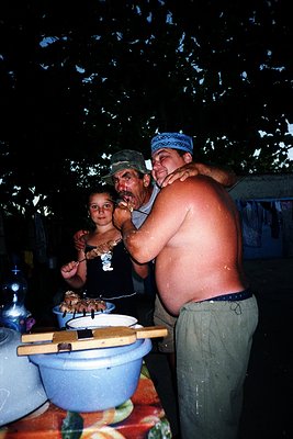 Family barbecue under night sky, likely 1970s–1980s. Two men and a woman prepare skewered meat at an outdoor gathering, with ...