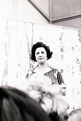 Mid-century woman in a striped blouse poses indoors, likely 1960s–1970s. Plain wall and floral-patterned curtain suggest dome...