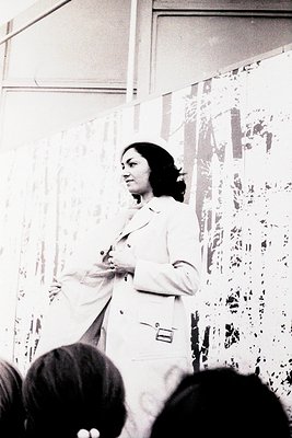 Mid-20th century medical professional in white lab coat addressing audience, likely a lecture or seminar. Decorated wall behi...