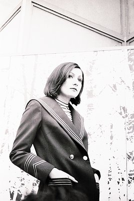 1960s-style naval-inspired blazer with gold piping and buttons. Indoor setting with classical architectural details. Short, l...