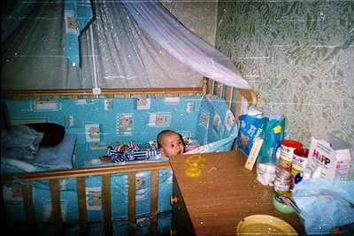 Vintage-style nursery featuring a wooden crib with blue floral bedding and a draped mosquito net. Infant peeks from under the...