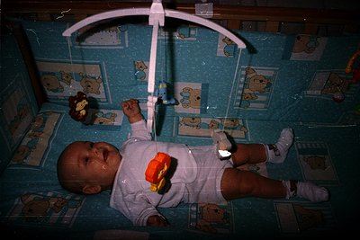 Vintage overhead baby swing with cartoon bear decals, mid-20th century design. Infant in diaper and onesie with orange/yellow...