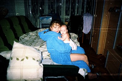 Tender moment captured indoors: a child in a blue tracksuit holds a baby in a matching outfit on a bed with floral-patterned ...