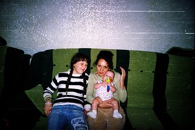 Vintage indoor portrait featuring two women and an infant on a green vinyl couch. The woman on the left wears a striped sweat...