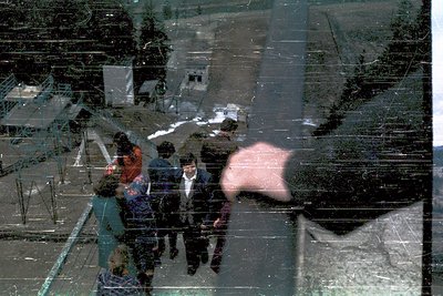 Reflection of three figures in winter attire—one in a dark coat, another in a patterned jacket—standing near a snow-covered r...