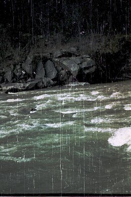 Nighttime river scene under heavy rain, illuminated by artificial light. Frozen waterfalls cascade over rocky terrain, blendi...