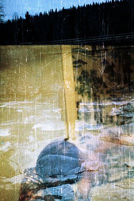 Reflection of a lone figure in rain-soaked glass, blurred by heavy precipitation. Urban setting with indistinct buildings and...