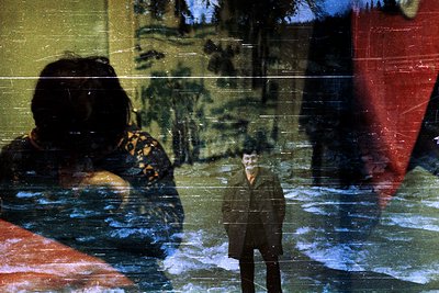 Vintage sepia-toned photo of a man in a suit standing on a snowy rooftop, reflected in a rain-streaked window. Blurred figure...