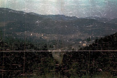Vintage aerial view of a forested valley with winding roads and scattered buildings, framed by a grid pattern (likely a slide...