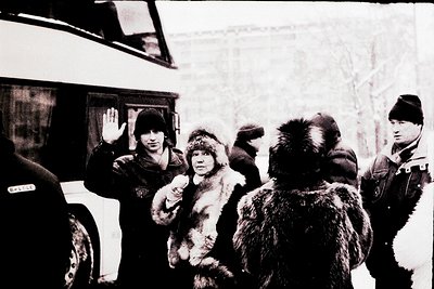 Cold winter scene featuring uniformed officers in fur-lined coats directing a child in a heavy fur parka. Snow-covered urban ...