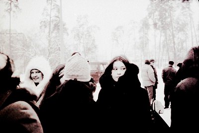 Vintage black-and-white photo of a winter gathering in a snow-covered forest. Group of people bundled in heavy coats, scarves...