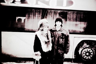 Black-and-white portrait of two individuals posing outside a bus with "BARD" partially visible on the signage. The woman wear...