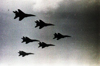 Five jet aircraft in tight formation, silhouetted against light sky. Likely Cold War-era jet fighters, possibly MiG-21 or sim...