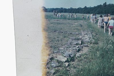 Vintage slide of a group hiking along a rocky, grassy trail in a rural landscape, likely 1960s–1970s. Casual attire suggests ...
