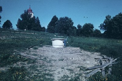 Vintage sepia-toned photo of a rural cemetery with a small white chapel in background. Central concrete mausoleum sits atop a...