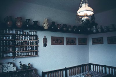 Vintage kitchen interior showcasing mid-20th-century domestic design. Wooden shelves hold glass jars, clay pots, and vintage ...