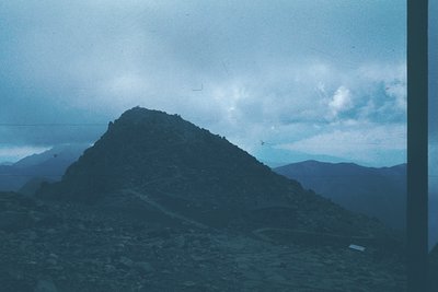 Vintage slide of rugged mountain peak under overcast skies, likely mid-20th century. Barren slopes and distant ridges suggest...