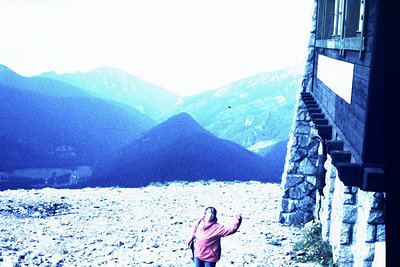 Vintage alpine hut framed by stone staircase, set against misty mountain peaks. Mid-20th century clothing suggests or . Rusti...