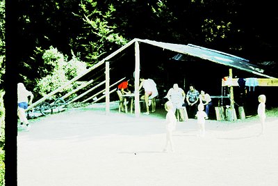Vintage outdoor playground with wooden structures under a shaded canopy. Children and adults play on swings, slides, and clim...