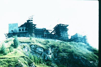Vintage black-and-white photo of a wooden fortress perched on rocky terrain, featuring multi-tiered watchtowers and ramparts....