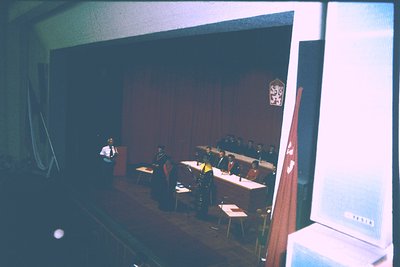 Vintage lecture hall featuring a speaker at a podium with a red curtain backdrop. Auditorium seating arranged in rows, with a...