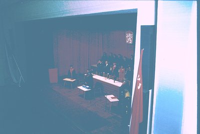 Formal conference table setup with red-and-white flag, coat of arms emblem, and draped curtains. Likely a government or offic...